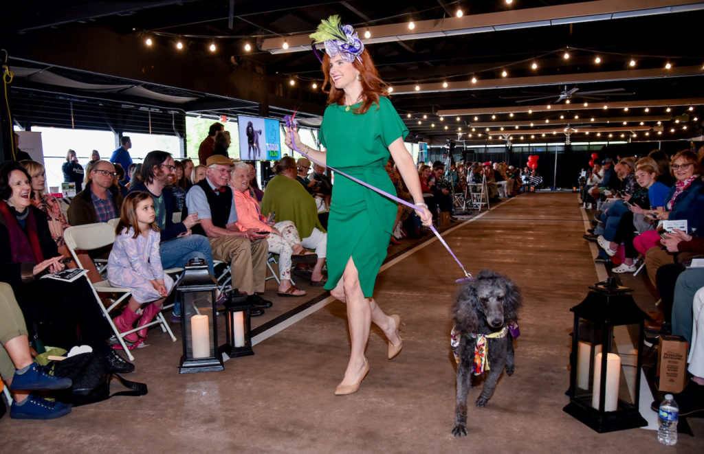 Model wearing Darrk green dress with Purple Fascinator and Poodle therapy pet